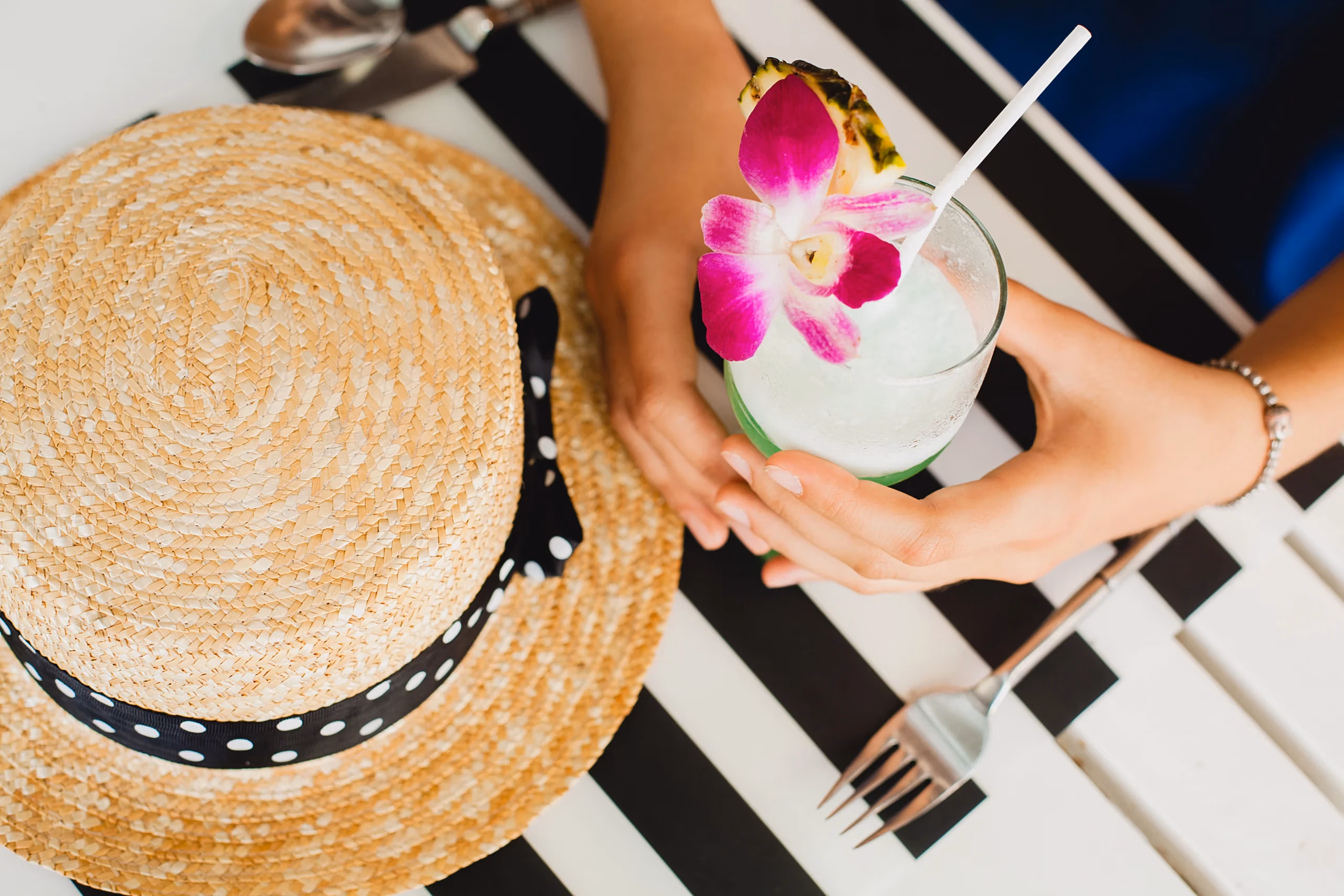 Attractive young woman blue dress straw hat wearing pink sunglasses drinking alcohol cocktail tropic